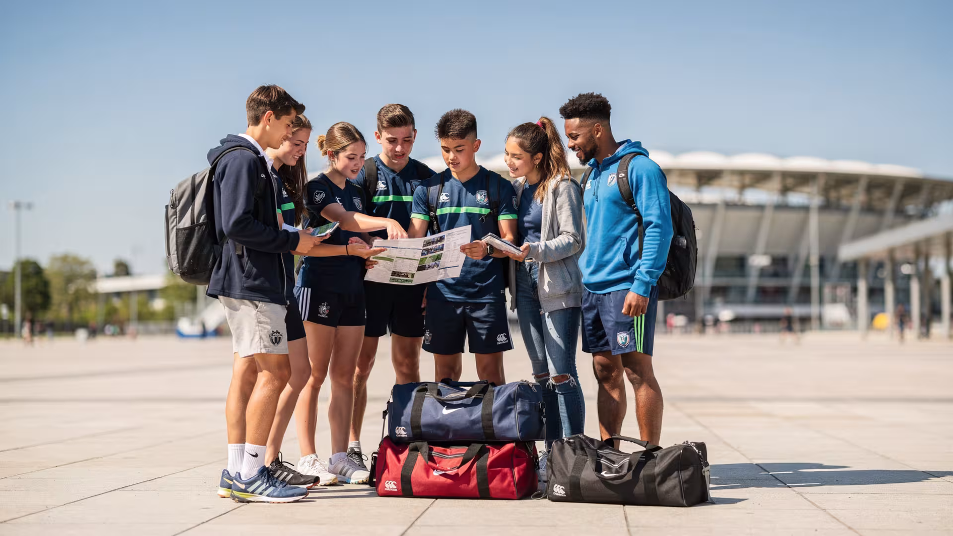 Young rugby players and coach reviewing a tour plan outside a stadium