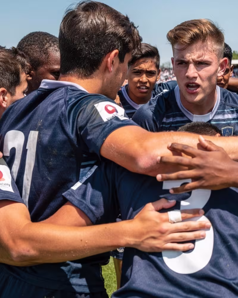 An all-male youth rugby team huddled together with a captain speaking before a match