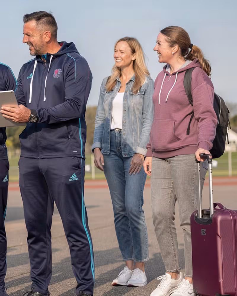 Coaches and tour coordinator helping a youth rugby team prepare beside a touring coach