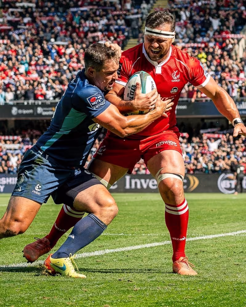 A rugby player breaking a tackle to power towards the try line as the crowd cheers