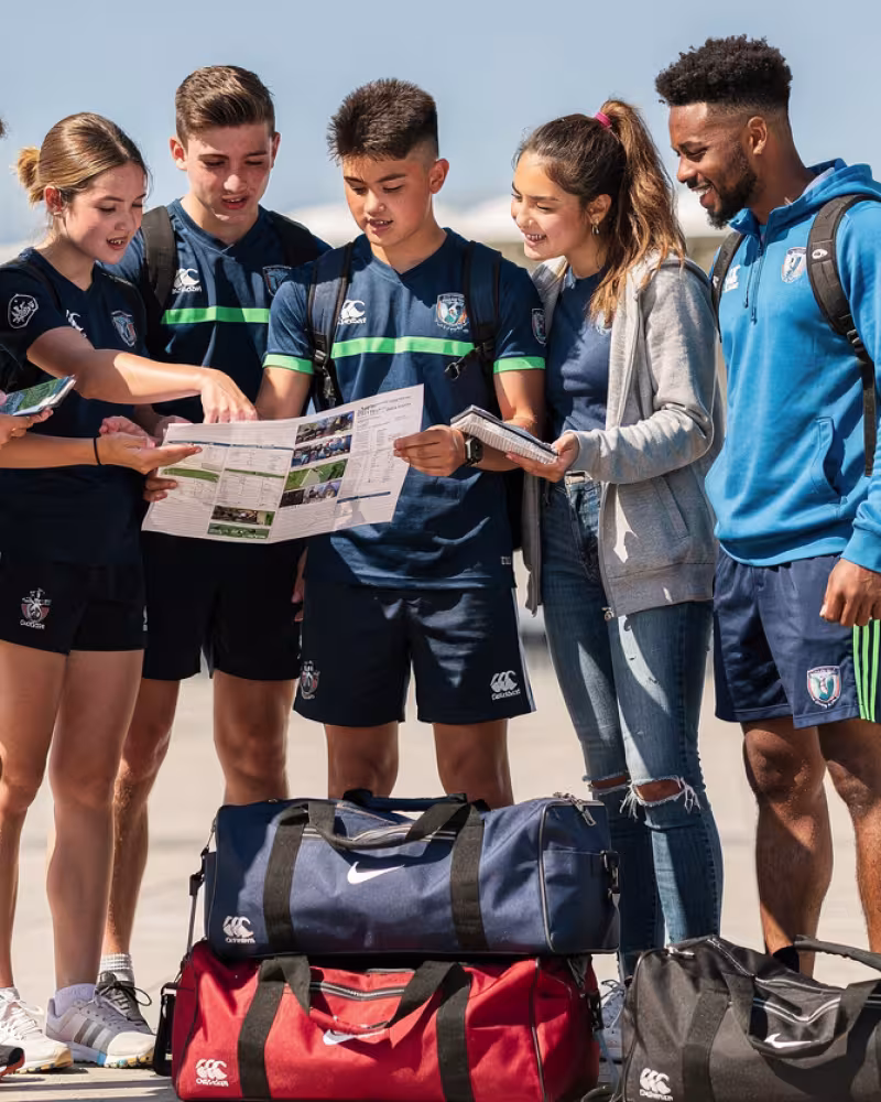 Young rugby players and coach reviewing a tour plan outside a stadium
