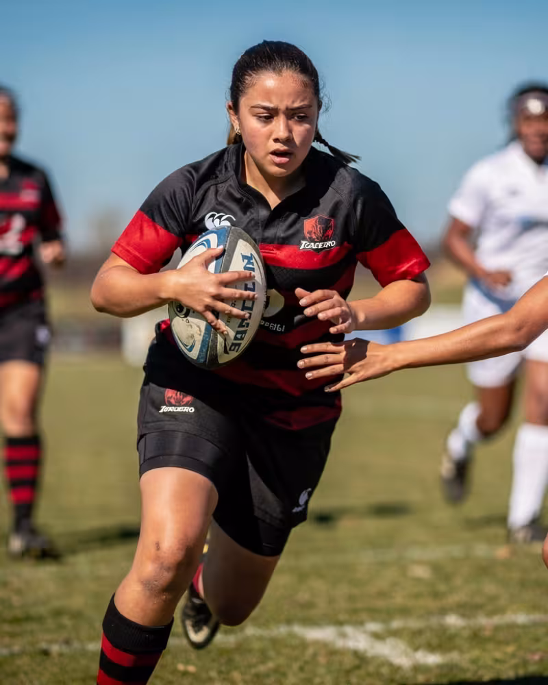 A 15-year-old girls rugby player running with the ball looking directly at the camera