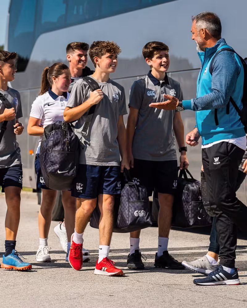 Teenage rugby players and coach arriving beside a team coach
