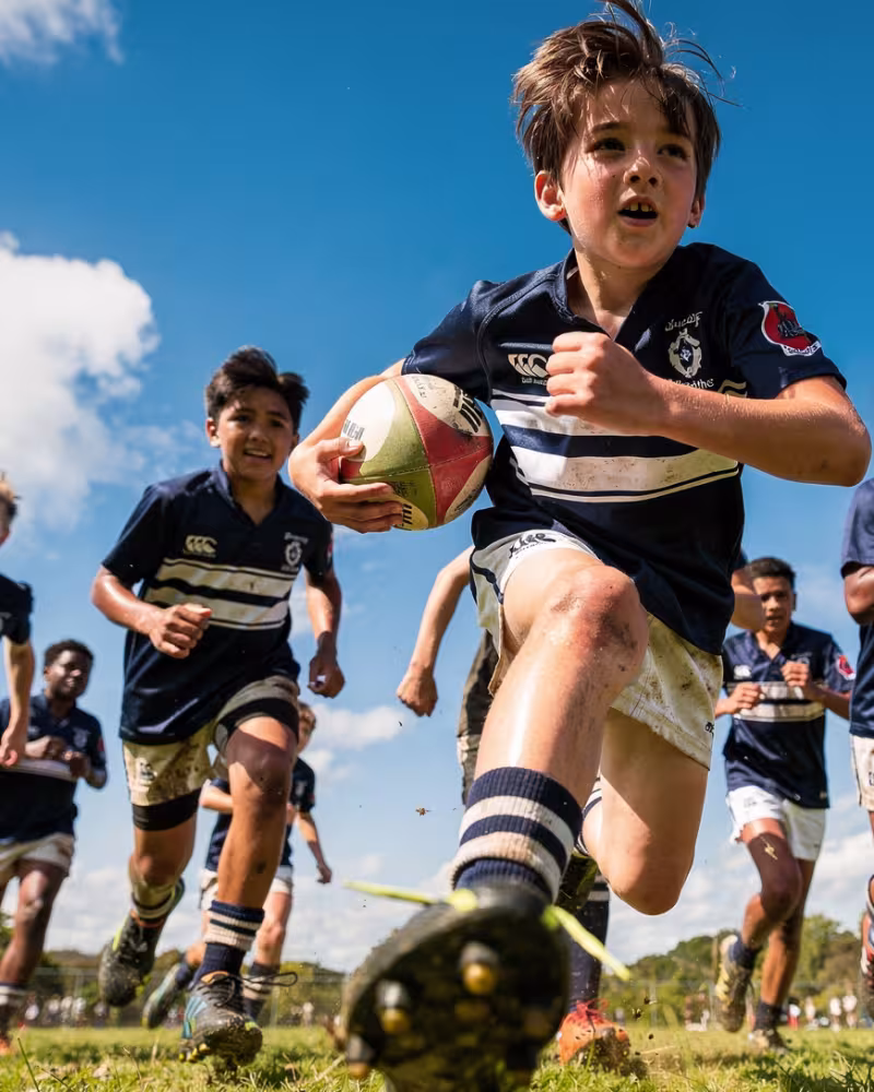 A young rugby player sprinting with the ball in a low-angle action shot, teammates following
