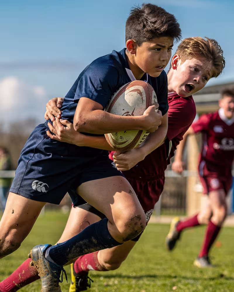 Youth rugby player breaking through a tackle in an away match