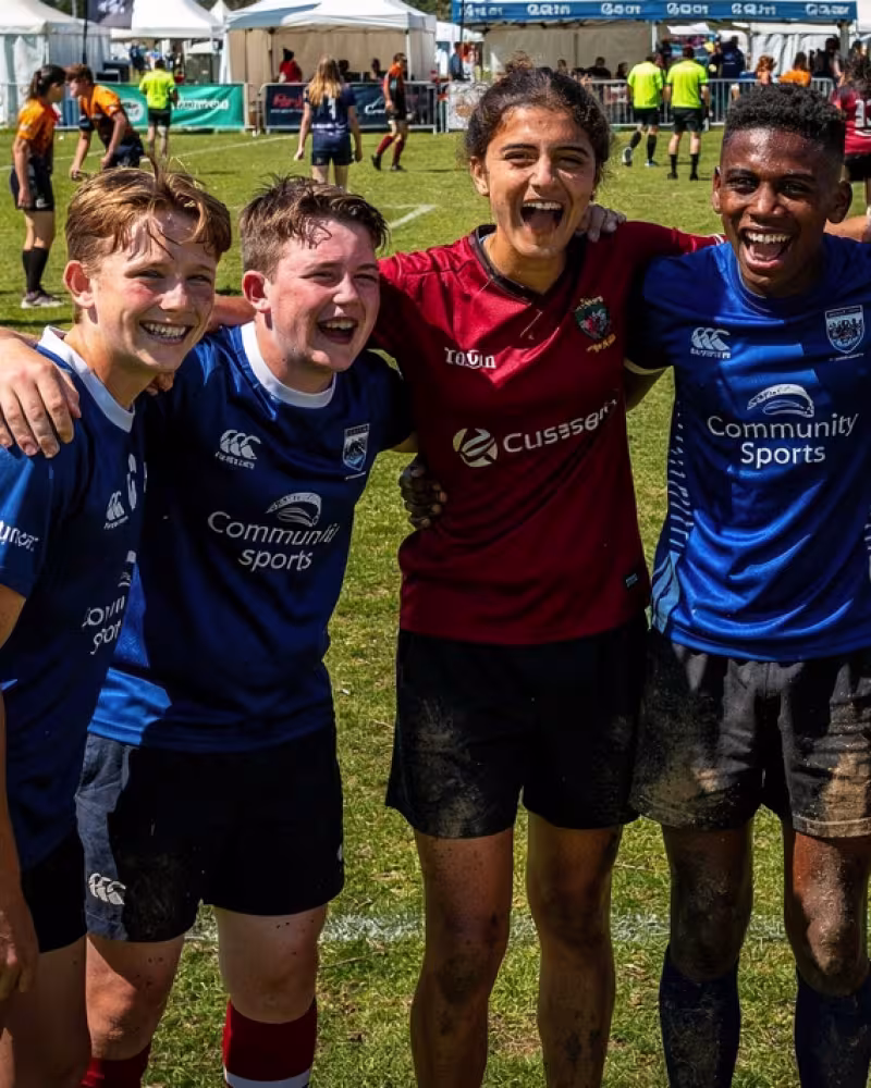 Youth rugby festival players celebrating together pitch-side, festival tents in the background